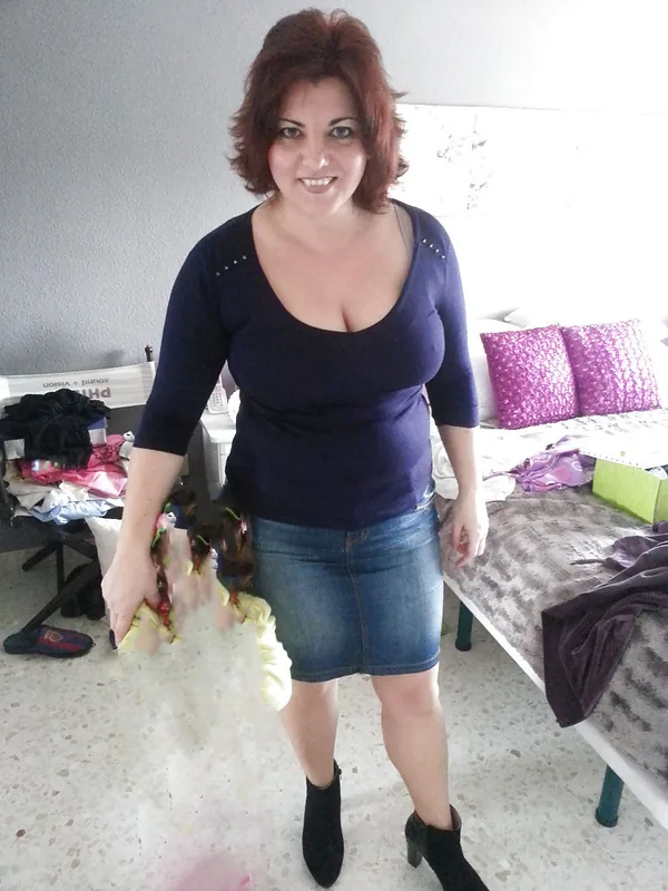 Femme souriante en haut bleu et jupe en jean tenant une poupée dans une chambre.