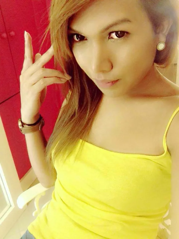 Portrait d'une jeune femme aux cheveux longs portant un haut jaune, regardant l'objectif devant un meuble rouge.
