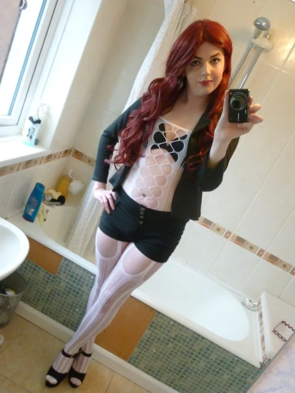 Femme aux cheveux roux prenant un selfie dans une salle de bain avec un appareil photo compact.